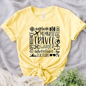 May include: Yellow t-shirt with black text that reads "Explore, Memories, Travel, Discover, Experience, Wander, Adventure, Fun, Culture". The text is arranged in a vertical column with a compass, airplane, camera, globe, suitcase, mountain, and sunglasses icons.