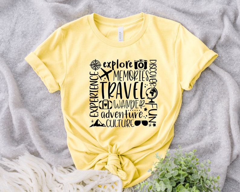 May include: Yellow t-shirt with black text that reads "Explore, Memories, Travel, Discover, Experience, Wander, Adventure, Fun, Culture". The text is arranged in a vertical column with a compass, airplane, camera, globe, suitcase, mountain, and sunglasses icons.