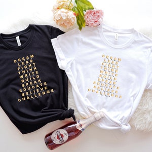 K&ouml;nnte beinhalten: Zwei T-Shirts mit den W&ouml;rtern "DREAM", "LEAD", "FIGHT", "THINK", "WRITE", "BUILD", "SPEAK", "EDUCATE", "BELIEVE" und "CHALLENGE", die in Form einer Pyramide auf der Vorderseite angeordnet sind. Die Shirts sind schwarz und wei&szlig;.