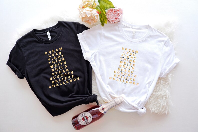 K&ouml;nnte beinhalten: Zwei T-Shirts mit den W&ouml;rtern "DREAM", "LEAD", "FIGHT", "THINK", "WRITE", "BUILD", "SPEAK", "EDUCATE", "BELIEVE" und "CHALLENGE", die in Form einer Pyramide auf der Vorderseite angeordnet sind. Die Shirts sind schwarz und wei&szlig;.