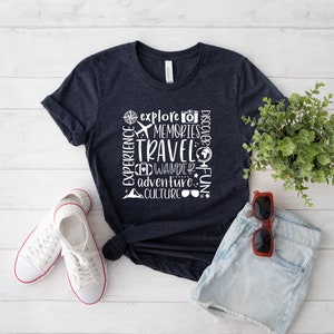 May include: A navy blue t-shirt with white text that reads "Experience, Explore, Memories, Travel, Wander, Discover, Adventure, Culture, Fun". The text is arranged in a vertical column with a compass, airplane, camera, and globe icons.
