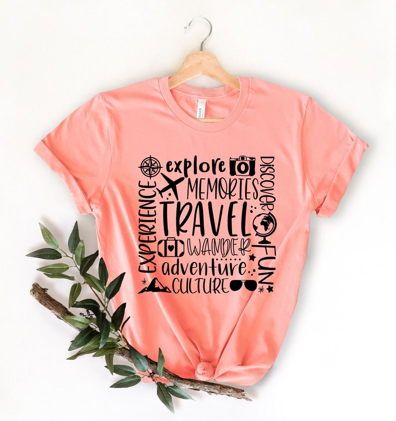 May include: A coral pink t-shirt with a black graphic design that says "Discover, Explore, Memories, Travel, Wander, Fun, Adventure, Culture".