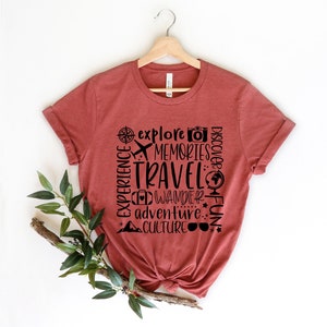 May include: A rust-colored t-shirt with a black graphic design that says "explore memories travel wander adventure culture fun" with travel-related icons.