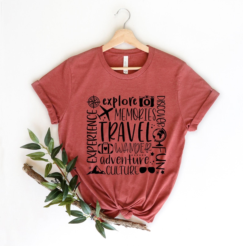 May include: A rust-colored t-shirt with a black graphic design that says "explore memories travel wander adventure culture fun" with travel-related icons.
