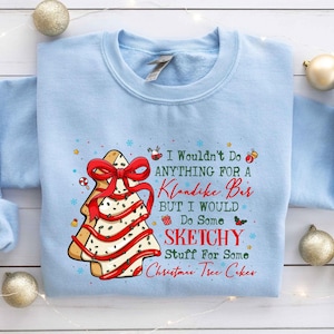 May include: Light blue sweatshirt with a Christmas tree cookie graphic. The cookie has a red bow and red stripes. Text on the sweatshirt reads "I Wouldn't Do Anything For a Klondike Bar But I Would Do Some Sketchy Stuff For Some Christmas Tree Cakes."