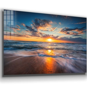 May include: A scenic photograph of a sunrise over the ocean. The sun is setting behind the horizon, casting a warm glow on the water and the sandy beach. The sky is a mix of blue, orange, and pink, with fluffy clouds.