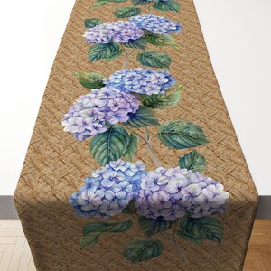 May include: A brown woven table runner with a border of blue and purple hydrangea flowers. The flowers are arranged in a vertical line down the center of the runner.