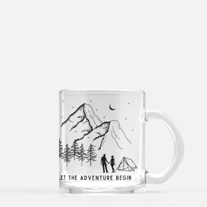 May include: A clear glass mug with a black and white illustration of a mountain range, a couple holding hands, and a tent. The text "Let the adventure begin" is printed on the bottom of the mug.