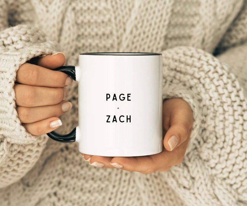 May include: White ceramic mug with a black rim and handle. The mug has the text "PAGE - ZACH" printed in black.