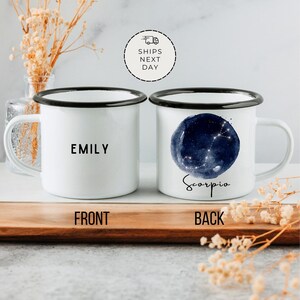 May include: White enamel mug with a black rim and handle. The front of the mug has the name "EMILY" printed in black. The back of the mug has a watercolor illustration of the Scorpio constellation with the word "Scorpio" printed below it.
