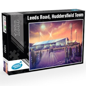 Könnte beinhalten: Ein 1000-teiliges Puzzle mit einem Gemälde eines Stadions bei Nacht. Das Stadion ist von Flutlichtern beleuchtet und es sind Menschen zu sehen, die draußen herumlaufen. Die Schachtel ist schwarz mit einem weißen Rand und der Text "Leeds Road, Huddersfield Town" ist auf der Vorderseite aufgedruckt.