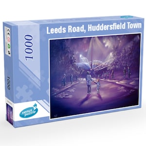 Könnte beinhalten: Eine blaue Schachtel mit einem 1000-teiligen Puzzle, das eine Nachtszene am Leeds Road, Huddersfield Town zeigt. Die Schachtel trägt den Text "Leeds Road, Huddersfield Town" und "1000" in Weiß. Das Bild zeigt einen Vater und seinen Sohn, die unter einem Scheinwerfer von einem Stadion weggehen.
