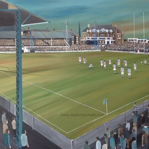 Puede incluir: Una pintura de un partido de fútbol que tiene lugar en un estadio. Los jugadores visten uniformes blancos y azules, y la multitud los anima. El estadio está rodeado por una valla, y hay árboles en el fondo. La pintura está firmada por el artista, "Phil Town".