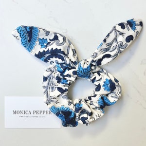 May include: A white scrunchie with a blue and gray floral pattern. The scrunchie has two long, floppy ends that are tied together in a bow.
