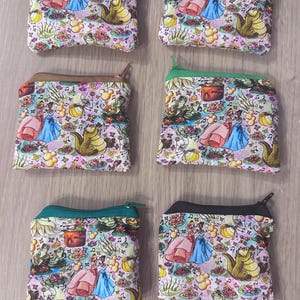 May include: Six small zippered pouches with a colourful print of a princess, a frog, and a crocodile. The pouches are made of fabric and have a zipper closure. The pouches are in different colours, including green, blue, brown, and black.