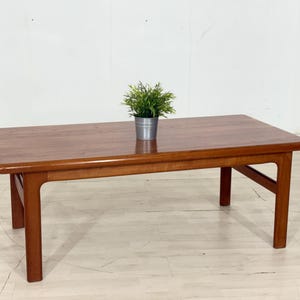 Peut inclure: Table basse rectangulaire en bois de style moderne du milieu du siècle. La table est de couleur marron chaud, avec des bords arrondis et quatre pieds robustes. Un petit pot de plante est posé sur la surface de la table, d'environ 120 cm de long.