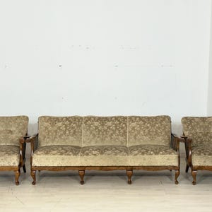Könnte beinhalten: Ein dreiteiliges Vintage-Wohnzimmer-Set mit einem Sofa mit floralem Muster und zwei passenden Sesseln. Das Set hat Holzrahmen und hellfarbene Polster. Die Sessel haben seitliche Details aus Korbgeflecht.
