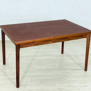 Op de afbeelding: Een rechthoekige houten tafel met een donkerbruin tafelblad en vier poten. De tafel heeft een eenvoudig, klassiek ontwerp, geschikt om te dineren of als bureau. De houtnerf is zichtbaar en draagt bij aan de natuurlijke uitstraling.