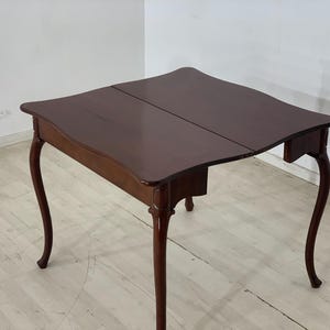 Op de afbeelding: Een donkerbruine houten klaptafel met een rechthoekig blad en vier poten. De tafel heeft een gebogen rand en een eenvoudig ontwerp.