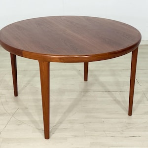 Peut inclure: Une table à manger ronde en bois avec un motif de grain brun riche. La table présente un plateau circulaire lisse et quatre pieds effilés qui s'étendent vers l'extérieur depuis le centre, offrant une base stable à la surface surélevée.