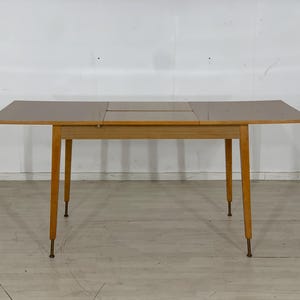 Peut inclure: Une table à manger extensible en bois clair avec un plateau rectangulaire et quatre pieds. La table a une finition brun clair et un design simple.