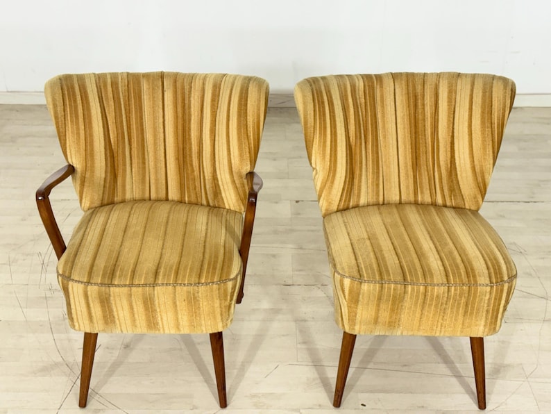 May include: Two vintage armchairs with a golden yellow, vertically striped fabric. The chairs have wooden legs and armrests. The design is mid-century modern, with a curved back and a low profile.