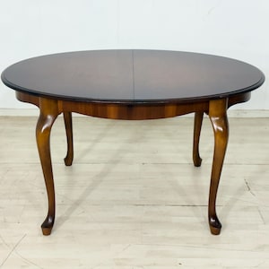 Op de afbeelding: Een ronde eettafel met een donkerbruin houten blad en een gladde, gepolijste afwerking. De tafel heeft vier gebogen cabriolepoten in een lichtere bruine houttint, die een stabiele basis vormen voor het cirkelvormige oppervlak.