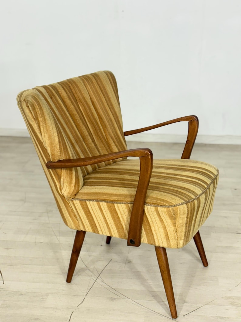May include: A vintage armchair with a striped pattern in shades of gold and brown. The chair features wooden armrests and legs, showcasing a mid-century modern design. The seat and back are upholstered with a textured fabric.