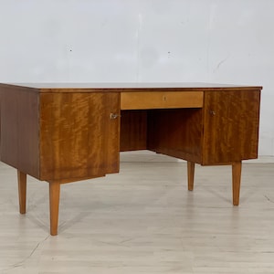 Könnte beinhalten: Ein vintage Holzschreibtisch mit zwei Schubladen und zwei Türen. Der Schreibtisch hat eine helle Holzoptik und ist in gutem Zustand.