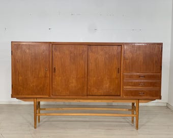Puede incluir: Un aparador de madera de estilo moderno de mediados de siglo con puertas correderas y cajones. El aparador está hecho de madera marrón claro y tiene un diseño simple y elegante.