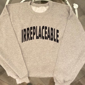 May include: A gray sweatshirt with the word "IRREPLACEABLE" printed in black on the front.