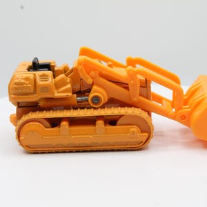 May include: Orange toy bulldozer with a black accent on top. The bulldozer has a front scoop and a track system for movement. The toy is made of plastic and is designed to resemble a construction vehicle.