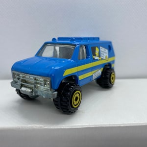May include: A blue toy van with yellow stripes and a cartoon character on the side. The van has black tires and a black grill.