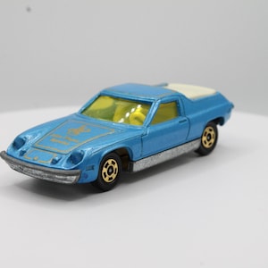 May include: A blue toy car with a white roof and gold accents. The car has a yellow steering wheel and black wheels.