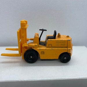 Pu&ograve; includere: Un carrello elevatore giocattolo giallo con ruote nere e un volante nero. Il carrello elevatore ha un sedile nero e dice "KOMATSU 650 5000" sul lato.