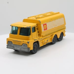 May include: A yellow toy truck with a Shell logo on the side. The truck has a large fuel tank and four wheels.