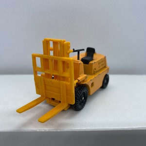 Pu&ograve; includere: Un carrello elevatore giocattolo giallo con ruote nere e un sedile nero. Il carrello elevatore ha una piattaforma rialzata con una gabbia di metallo.