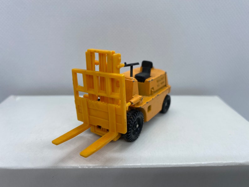 Pu&ograve; includere: Un carrello elevatore giocattolo giallo con ruote nere e un sedile nero. Il carrello elevatore ha una piattaforma rialzata con una gabbia di metallo.