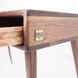 Peut inclure: Un bureau en bois avec un tiroir partiellement ouvert. Le bureau est en bois de noyer et porte une plaque en laiton avec le texte "Diaz Marentes Studio" sur le côté.