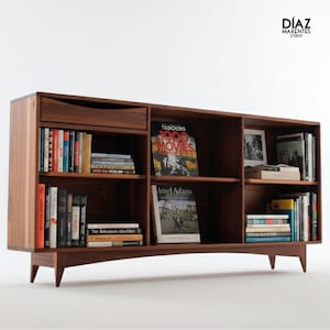 May include: A dark brown wooden bookshelf with a drawer and multiple shelves filled with books. The bookshelf has a mid-century modern design with angled legs and a clean, minimalist aesthetic. The text "Díaz Marentes Studio" is in the upper right corner.