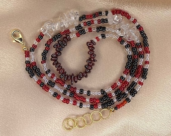 May include: A multi-strand beaded necklace with red, black, and white beads. The necklace has a gold clasp and clear crystal beads.
