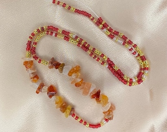 May include: A beaded waist chain with red, gold, and white beads. The chain also features a strand of orange, brown, and white gemstone beads.