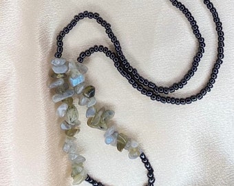 May include: A necklace with a black beaded chain and a long strand of light gray and blue gemstone beads.