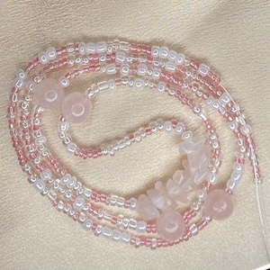 May include: A pink and white beaded necklace with rose quartz beads. The necklace is made of multiple strands of beads and has a variety of shapes and sizes.