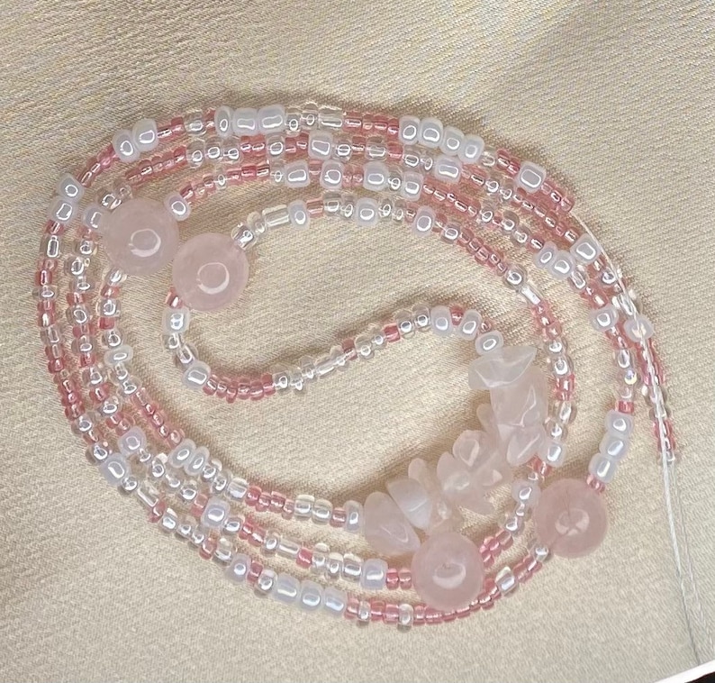 May include: A pink and white beaded necklace with rose quartz beads. The necklace is made of multiple strands of beads and has a variety of shapes and sizes.
