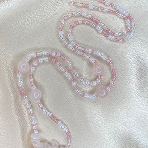May include: A pink and white beaded necklace with rose quartz beads. The necklace is made with small, round beads and larger, irregular shaped rose quartz beads.