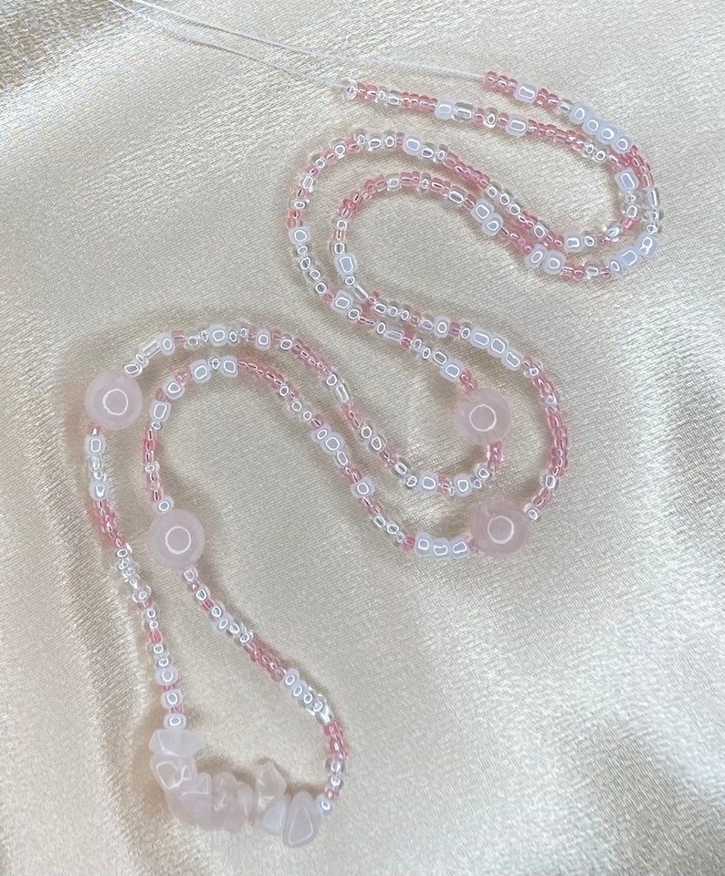 May include: A pink and white beaded necklace with rose quartz beads. The necklace is made with small, round beads and larger, irregular shaped rose quartz beads.