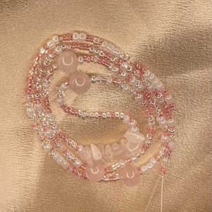 May include: A pink and white beaded necklace with rose quartz beads. The necklace is made of multiple strands of beads and has a variety of shapes and sizes.
