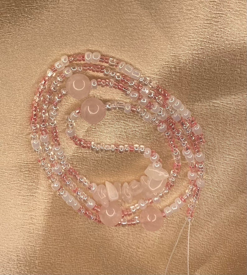 May include: A pink and white beaded necklace with rose quartz beads. The necklace is made of multiple strands of beads and has a variety of shapes and sizes.