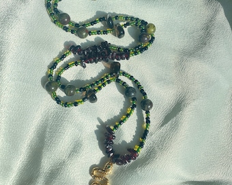 May include: A multi-strand beaded necklace featuring small black, green, and yellow seed beads interspersed with larger round stone beads and dark red irregular chip beads. A gold-toned snake pendant hangs from the bottom with a lobster clasp.